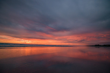 Fototapeta na wymiar Muriwai Beach at sunset time with colorful clouds, New Zealand