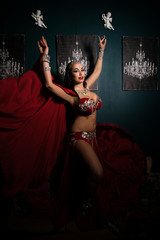 Sexy slim woman, belly dancer in red costume with crystals. Dark background