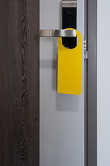 Room label tag hotel sign hanging on modern metal doorknob handle on wooden door with workspace for your own writing and design