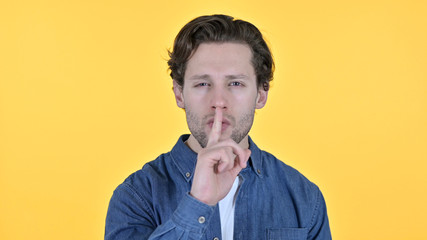 Young Man with Finger on Lips, Quiet Sign on Yellow Background