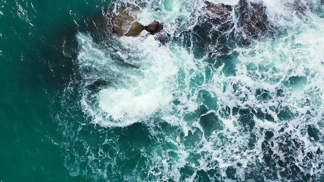 Caribbean rocky coast and rough emerald sea splashing on the stones. Aerial vertical background of a dangerous stormy ocean