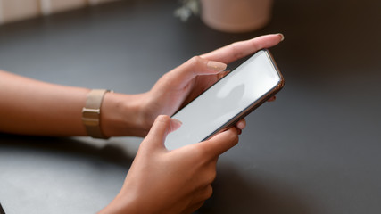 Cropped shot of college girl typing on mock-up smartphone on black table