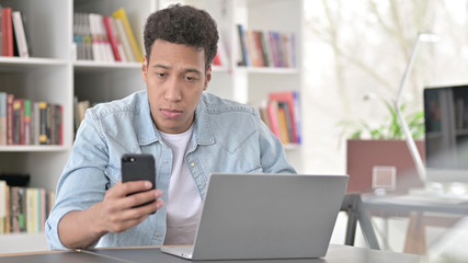 Young African American Man Working on Smartphone and Laptop