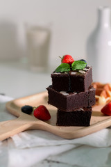 Cropped shot of stack chocolate brownies  with strawberries and blueberries decorated on wooden tray