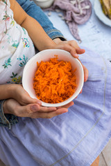 Raw orange Korean carrot salad in young girl hands with mother hands. Hold together. Family food concept