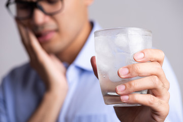 Young man with sensitive teeth and hand holding glass of cold water with ice. Healthcare concept.