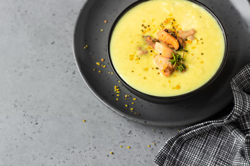 Bowl with thick clam chowder, decorated with seafood, thyme and pepper. Grey stone background. 