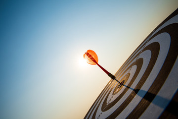 Close up shot red darts arrows in the target center on dark blue sky background. Business target or...