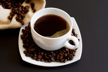 coffee beans in a bag with a white Cup of fresh coffee on a black background. space for text, top view.