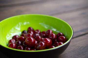 Ripe red and cherries in green bowl on wooden table. Summer delicacy with sweet berries in the countryside.