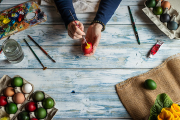 Hands painting Easter eggs on white wooden table, top view