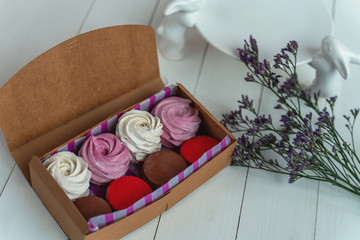 Gift set of sweets from macarons and marshmallows beautifully photographed in a box on a white wooden table with flowers