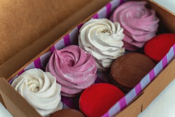 Gift set of sweets from macarons and marshmallows beautifully photographed in a box on a white wooden table with flowers