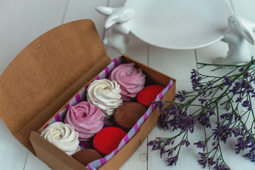 Gift set of sweets from macarons and marshmallows beautifully photographed in a box on a white wooden table with flowers