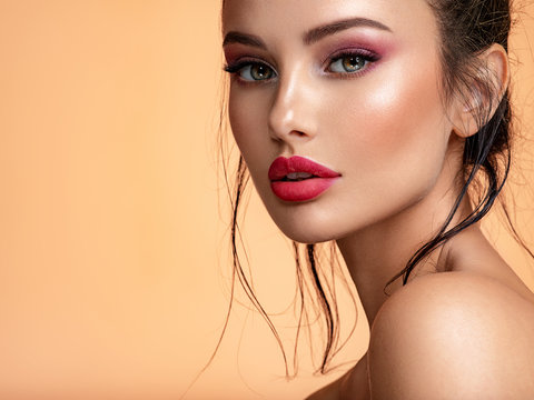 Beautiful white girl with red lips looks to the camera. Stunning brunette girl. Closeup face of young beautiful woman with a healthy clean skin. Pretty woman with bright  makeup of eyes.