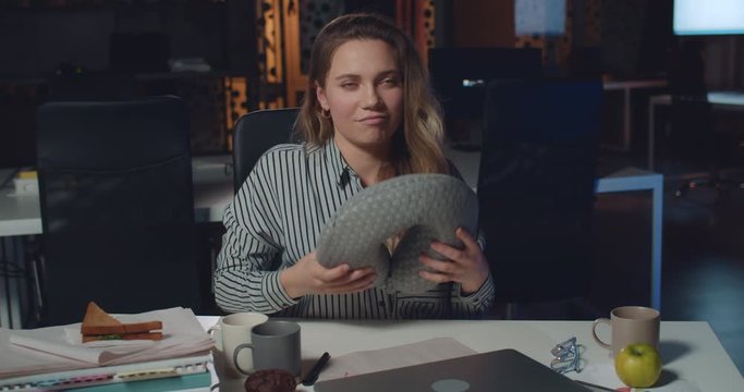 Satisfied businesswoman closing her laptop, wearing neck pillow and trying to sleep. Young woman office worker finishing her work on computer and sleeping at workplace. Concept of workaholism