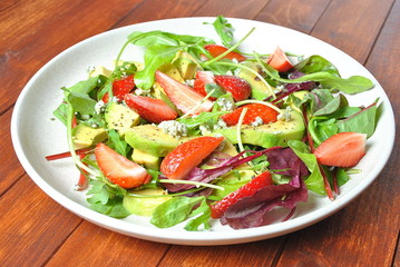 Avocado salad with strawberries, blue cheese, arugula and beet leaves on wooden background. Healthy lunch bowl Vegan healthy food concept
