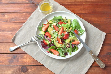 Avocado salad with strawberries, blue cheese, arugula and beet leaves on wooden background. Healthy lunch bowl Vegan healthy food concept