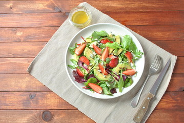 Avocado salad with strawberries, blue cheese, arugula and beet leaves on wooden background. Healthy lunch bowl Vegan healthy food concept