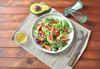 Avocado salad with strawberries, blue cheese, arugula and beet leaves on wooden background. Healthy lunch bowl Vegan healthy food concept