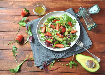 Avocado salad with strawberries, blue cheese, arugula and beet leaves on wooden background. Healthy lunch bowl Vegan healthy food concept