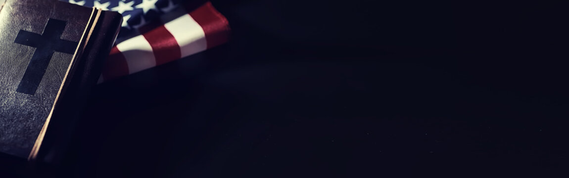 American flag and holy bible book on a mirror background. Symbol of the United States and religion. Bible and striped flag on a black background. - Powered by Adobe