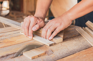 Close up, carpenter man cutting a plank of wood in the working using a circular saw in workshop.