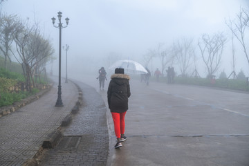 Female tourist with umbrella walking on misty road in Sapa, Vietnam