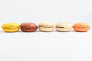 Five sweet French macarons with different aromas, isolated on white, flavours of strawberries, lemon, caramel, vanilla, orange and chocolate, tasty dessert in pastel colors on a table