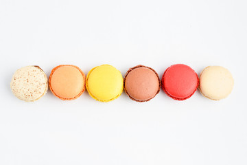 Top view of row of six sweet French macarons with different aromas, isolated on white, flavours of lemon, caramel, vanilla, orange and chocolate, tasty dessert in pastel colors on a table