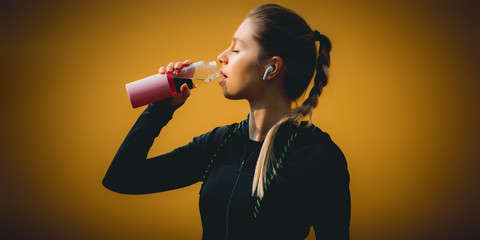 Girl in the sport suit training run in the park in cold weather and drinking to refuel her energy and keep workout stay healthy with wireless headphones in her ear to listening the music