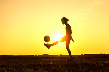 Boy playing with ball in nature in hot evening, silhouette of playing child at sunset in countryside