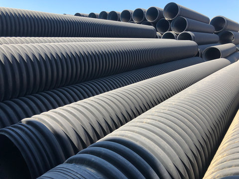 Stacked corrugated pvc-pipes at the outdoor warehouse. Drainage, plumbing, stormwater equipment