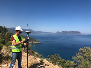 Geodetic engineer surveyor in white hard hat doing measurements with GNSS satellite receiver at the...