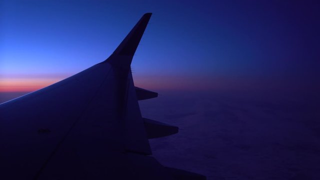 Through the porthole, you can see the wings of the aircraft , which is in the air against the background of clouds, and navigation lights are flashing on the wing. Traveling by plane , night flight, y