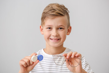 Little boy with contact lens case and eyeglasses on grey background