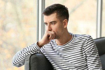Depressed young man near window at home