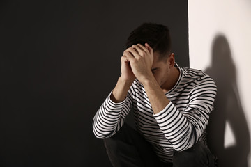 Depressed young man sitting near wall