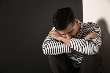 Depressed young man sitting near wall