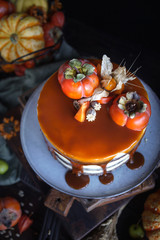 Autumn cake with persimmon and caramel with a pumpkin and a girl in a burgundy dress on a black background, Atmospheric dark food photos, Pastry Homemade in Womans hands, Selective focus