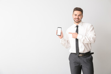 Young businessman with mobile phone on light background