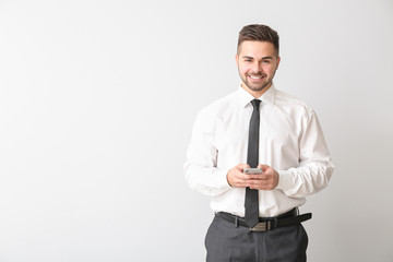 Young businessman with mobile phone on light background