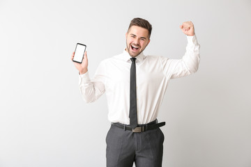 Happy businessman with mobile phone on light background