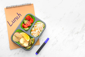 School lunch box with tasty food and notebook on light background