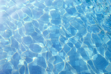 Tile floor of swimming pool with moving surface of chlorine water and reflection of sunlight