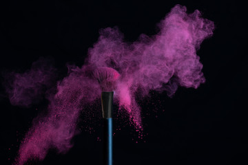Make-up brush with pink powder explosion isolated on a black background