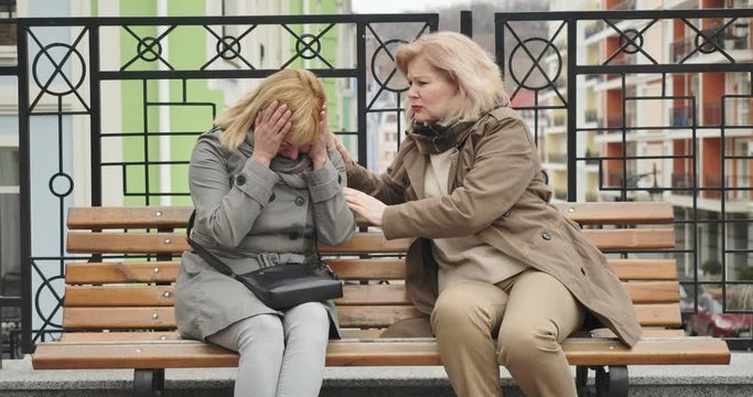 Crying senior Caucasian woman complaining to friend outdoors. Middle-aged blond retiree supporting depressed stressed lady. Problems, distraught, help, friendship. Cinema 4k ProRes HQ.