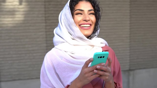 Young Muslim woman wearing hijab texting message with her smartphone.