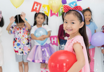 Fototapeta na wymiar happy birthday children Asian girls hug red balloons and friends in Living room smiling to camera. group of Asian ethnicity children model. concept of kids celebrate birthday party together