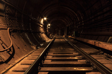A lighted reinforced concrete subway tunnel, cable routes are laid, the railroad tracks turn left. In front of them are iron vertical boxes of automatics.